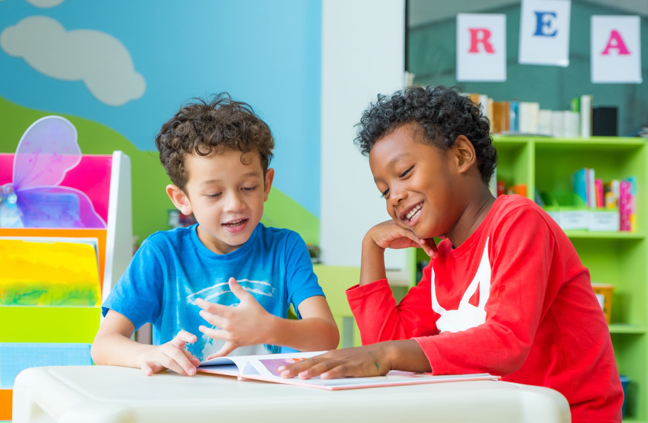 two young boys reading a book in a colorful classroom.